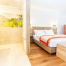 Modernes Hotelzimmer mit Doppelbett, orangefarbenem Sessel und offener Dusche.