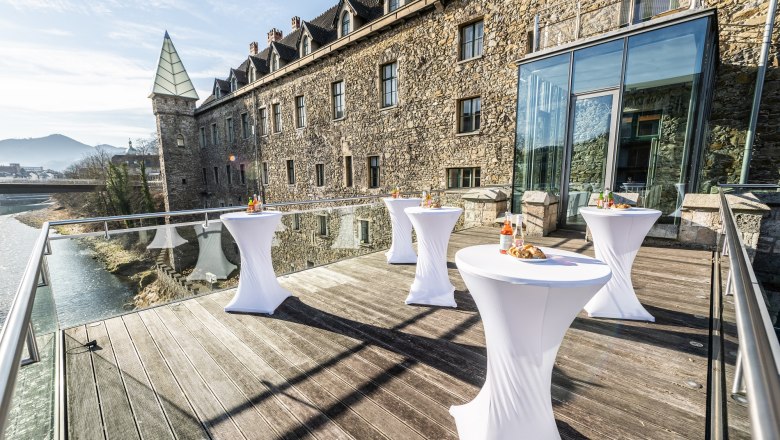 Terrasse mit Stehtischen vor einem historischen Geb&auml;ude mit Glasfassade.