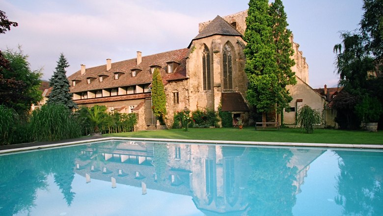 Historisches Gebäude mit Pool im Vordergrund, umgeben von Bäumen und Garten.