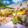 Gastgarten am Abend mit Beleuchtung und vielen Sitzm&ouml;glichkeiten, Pflanzen und Schirmen.