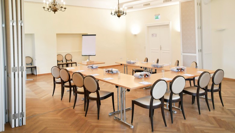 Konferenzraum mit Tischen und St&uuml;hlen, Flipchart und Kronleuchter.