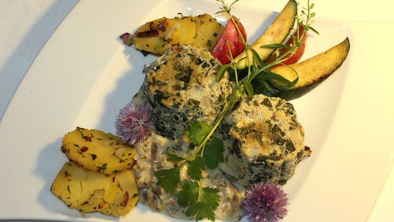 Ein Teller mit Spinatkn&ouml;deln, Kartoffeln und Gem&uuml;se dekorativ angerichtet.