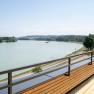 Holzterrasse mit Blick auf einen Fluss und gr&uuml;ne Landschaft.