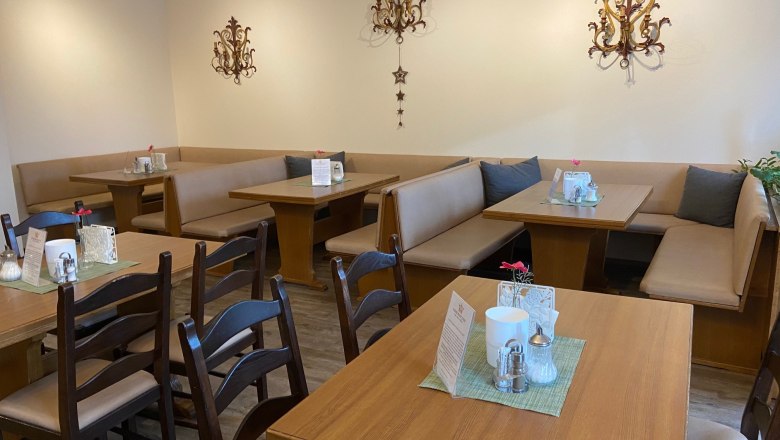 Gem&uuml;tlicher Fr&uuml;hst&uuml;cksbereich mit Holztischen und gepolsterten Sitzb&auml;nken, dekoriert mit Wandornamenten.