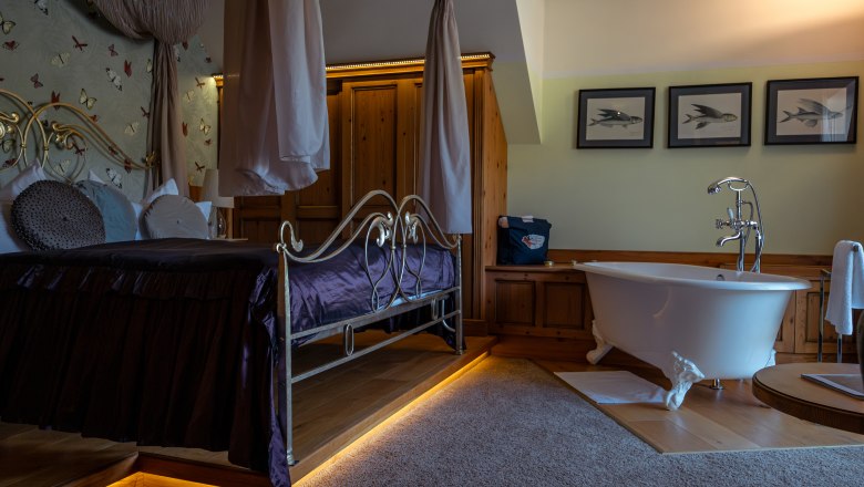 Luxuri&ouml;ses Hotelzimmer mit Himmelbett und freistehender Badewanne.