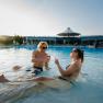 Zwei Personen entspannen im Pool des Thermenresorts Laa und sto&szlig;en mit Weingl&auml;sern an.
