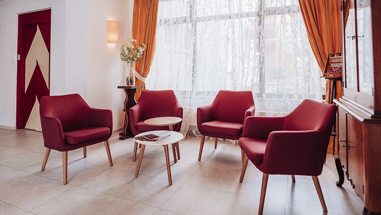 Gem&uuml;tliche Sitzecke mit roten Sesseln und kleinem Tisch vor einem Fenster mit Vorh&auml;ngen.