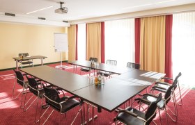 Konferenzraum mit U-f&ouml;rmigem Tisch, St&uuml;hlen, Flipchart und Projektor.