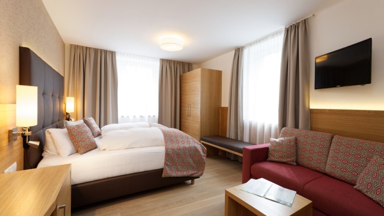 Modernes Hotelzimmer mit Doppelbett, Sofa, Schrank und Fernseher.