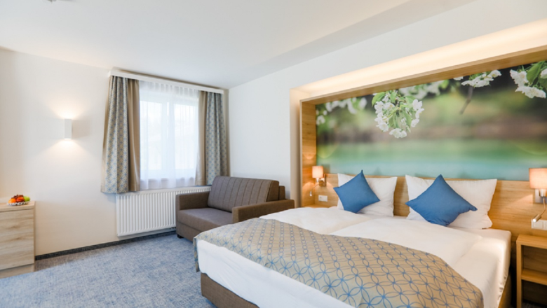Modernes Hotelzimmer mit Doppelbett, Sofa und gro&szlig;em Wandbild mit Blumenmotiv.