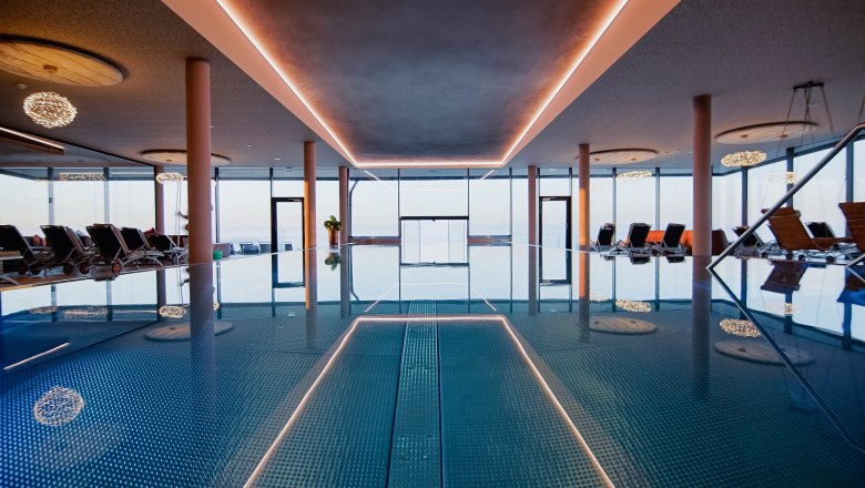 Innenansicht eines Infinitypools mit Liegest&uuml;hlen und gro&szlig;en Fenstern.