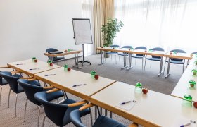 Konferenzraum mit Tischen in U-Form, Stühlen, Flipchart und Schreibmaterialien.