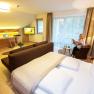 Modernes Hotelzimmer mit Doppelbett, Schreibtisch, Fernseher und Frau, die Zeitung liest.