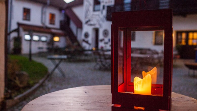 Laterne mit brennender Kerze auf einem Holztisch im Innenhof eines Landhotels.