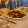 Ein Teller mit Fleisch, Gem&uuml;se und Kartoffeln auf einem Tisch, daneben ein Glas Wei&szlig;wein.