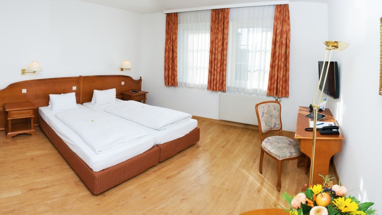 Ein gem&uuml;tliches Doppelzimmer mit zwei Betten, Holzm&ouml;beln und einem Schreibtisch mit Stuhl.