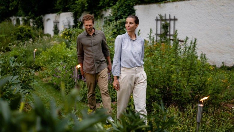 Ein Mann und eine Frau spazieren durch einen gr&uuml;nen Garten, umgeben von Pflanzen.