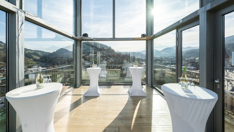 Innenansicht eines modernen Glasraums mit Stehtischen und Bergblick.