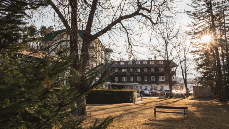 Hotel Schneeberghof im Sonnenlicht mit Bäumen im Vordergrund.