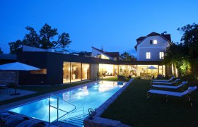 Abendansicht eines modernen Hotels mit beleuchtetem Pool und Liegest&uuml;hlen im Garten.