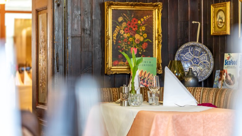 Gem&uuml;tlich gedeckter Tisch in einem rustikalen Restaurant mit Blumenbild und Dekorationen an der Wand.