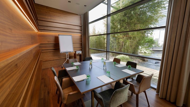 Moderner Meetingraum mit Holzw&auml;nden, gro&szlig;em Tisch und Blick auf einen Garten.