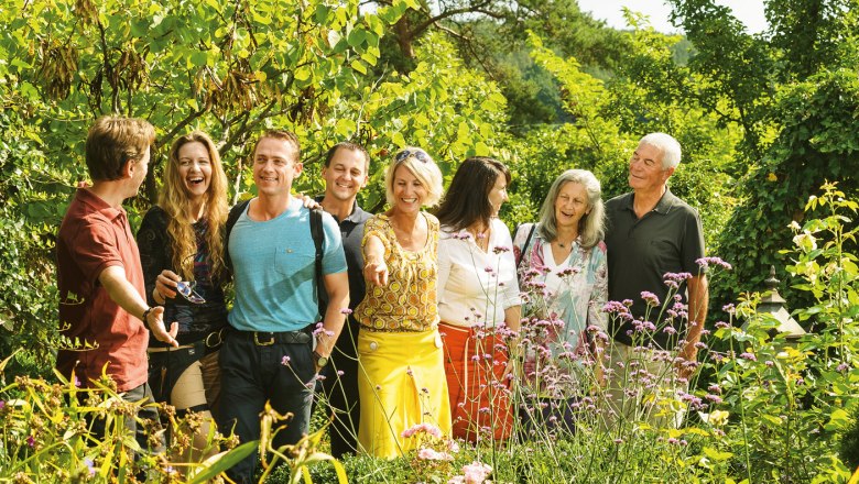Eine Gruppe von Menschen steht lächelnd in einem blühenden Garten.