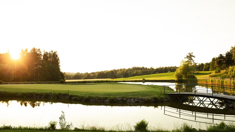 Golfplatz mit Teich und Brücke bei Sonnenuntergang im Golfresort Haugschlag.