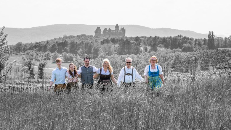 Eine Gruppe von sechs Personen in traditioneller Kleidung steht auf einem Feld mit einer Burg im Hintergrund.