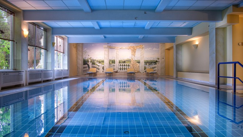 Innenansicht eines Hallenbads mit blauem Wasser und Wandgemälde.