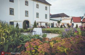 Gartenansicht von Schloss Raggendorf mit Blumen, Tischen und Stühlen im Vordergrund.