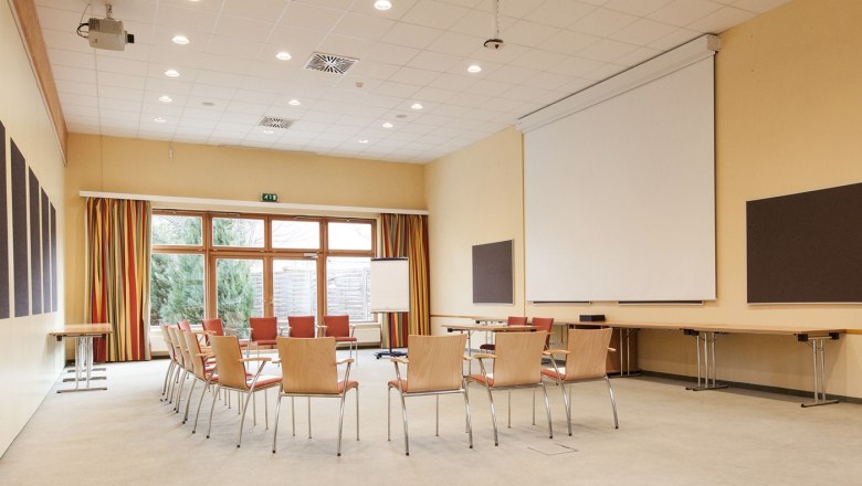 Ein leerer Seminarraum mit Stuhlkreis, Beamer, Leinwand und Flipchart.