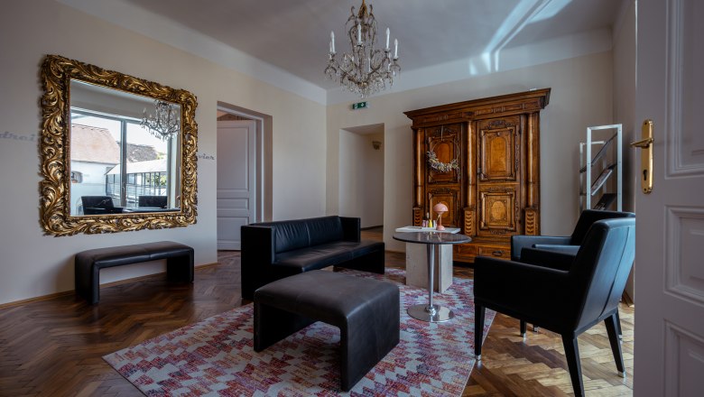 Elegantes Wohnzimmer mit antikem Schrank, gro&szlig;em Spiegel, schwarzen Lederm&ouml;beln und einem Kronleuchter.