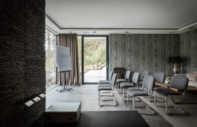 Moderner Konferenzraum mit grauen Stühlen, Flipchart und großen Fenstern.