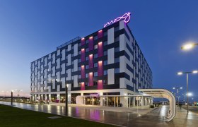 Au&szlig;enansicht des Moxy Vienna Airport Hotels bei D&auml;mmerung mit beleuchtetem Schriftzug.