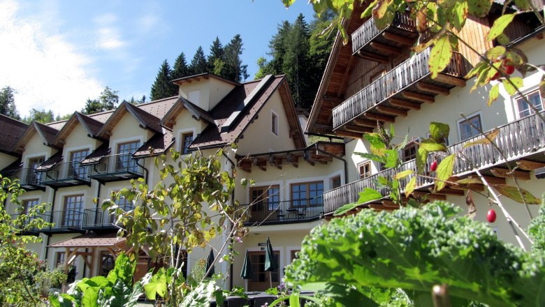 Ein Geb&auml;ude im alpinen Stil mit Balkonen, umgeben von &uuml;ppigem Gr&uuml;n und Pflanzen.