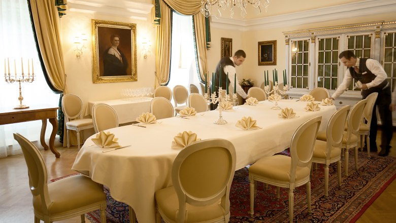 Eleganter Speisesaal mit gedecktem Tisch, Kerzenleuchtern und zwei Kellnern.