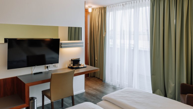 Modernes Hotelzimmer mit Schreibtisch, Fernseher und Vorhängen.