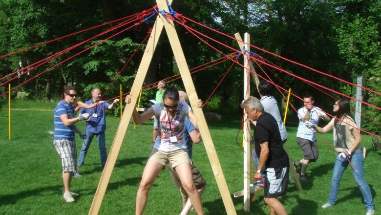 Menschen bei einem Teambuilding-Event im Freien mit Holzstruktur und Seilen.