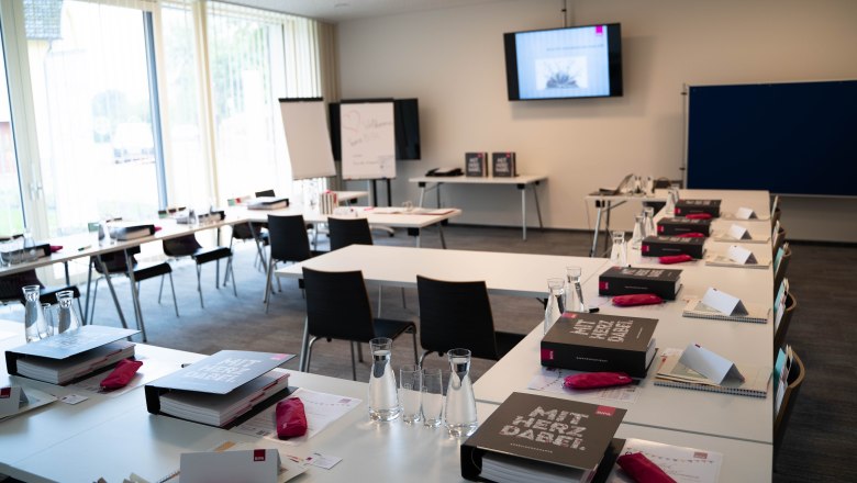 Ein Seminarraum mit Tischen, Stühlen, Ordnern und Wasserflaschen, bereit für eine Veranstaltung.