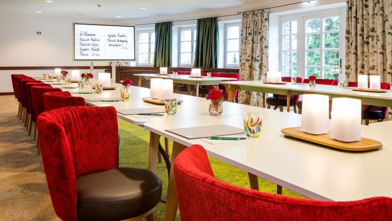 Eleganter Seminarraum mit roten Stühlen und weißen Tischen.