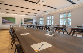 Seminarraum im Hotel Spitzerberg mit langen Holztischen, Stühlen, Wasserflaschen und Schreibmaterialien.