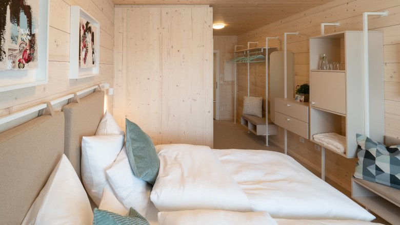 Modernes Doppelzimmer mit Holzw&auml;nden, Bett, Kissen und minimalistischer Einrichtung.