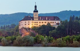 Schloss Persenbeug auf einem Hügel mit Fluss im Vordergrund.