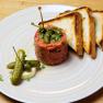 Beef Tartar mit Kapern, Gew&uuml;rzgurken und Toast auf einem Teller.