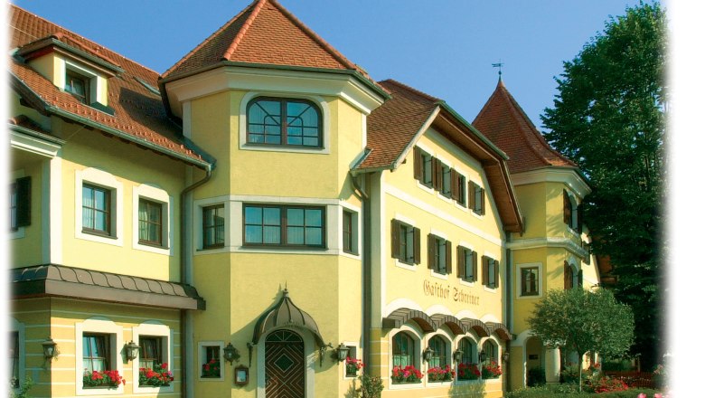 Gelbes Gebäude mit roten Dächern und vielen Fenstern, umgeben von Bäumen.