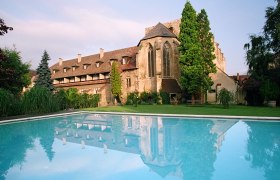 Historisches Gebäude mit Pool im Vordergrund, umgeben von Bäumen und Garten.